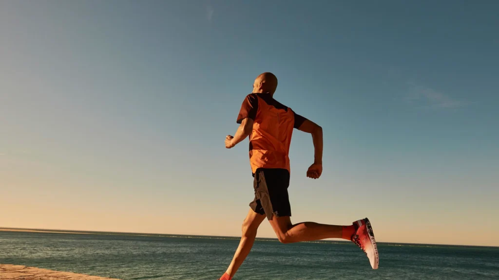 Runner in corsa lungo il mare al tramonto, simbolo di prevenzione e benessere osteopatico e fisioterapico.