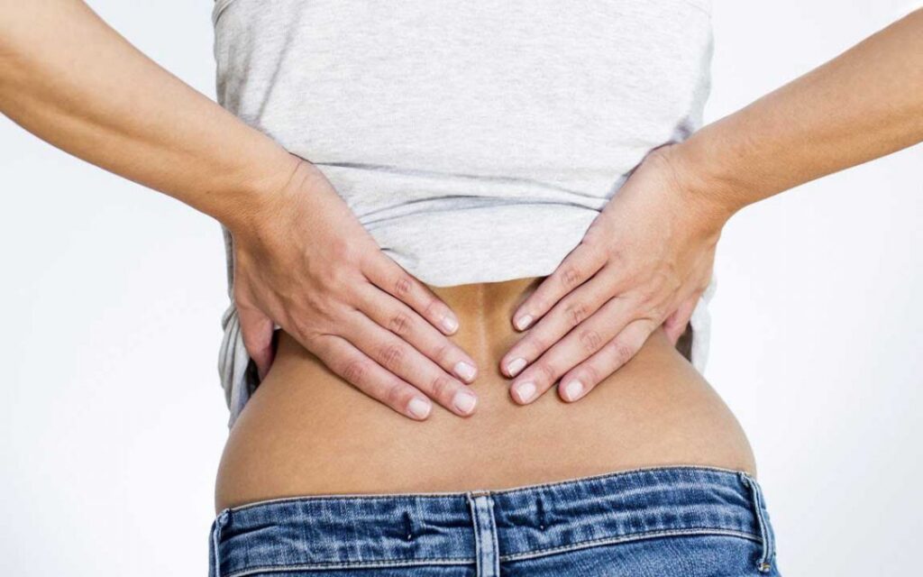 Donna con dolore alla schiena che si tiene la zona lombare, rappresentando il disagio della lombalgia e la necessità di trattamenti osteopatici.